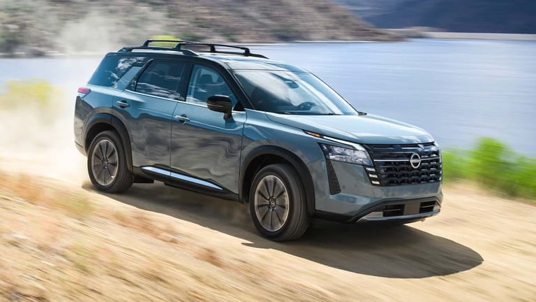 Blue Nissan Pathfinder SUV driving on sandy terrain with roof rack and water visible in background